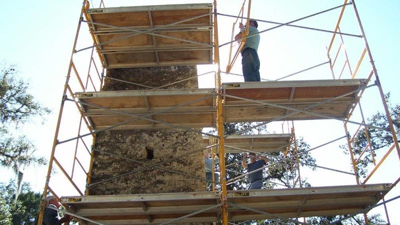 a man stands on several wooden scaffolds surrounding an aged stone chimney